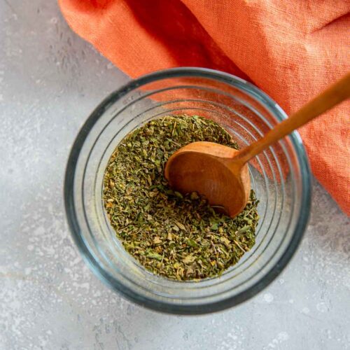 small glass jar of seasonings with wooden spoon stirring