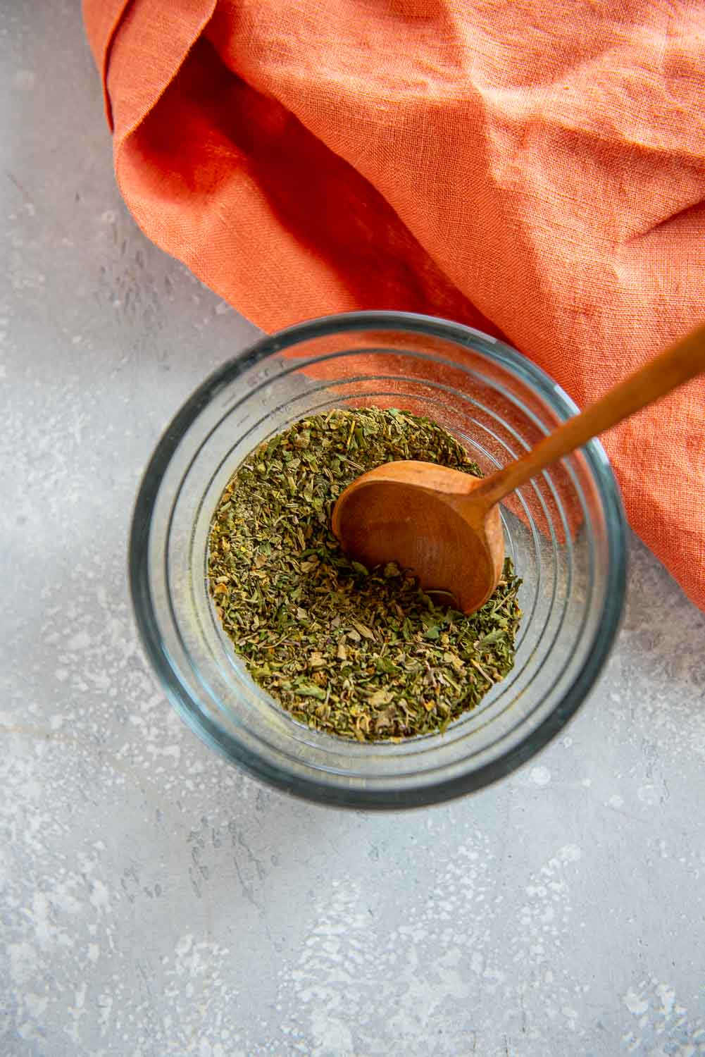 small glass jar of seasonings with wooden spoon stirring