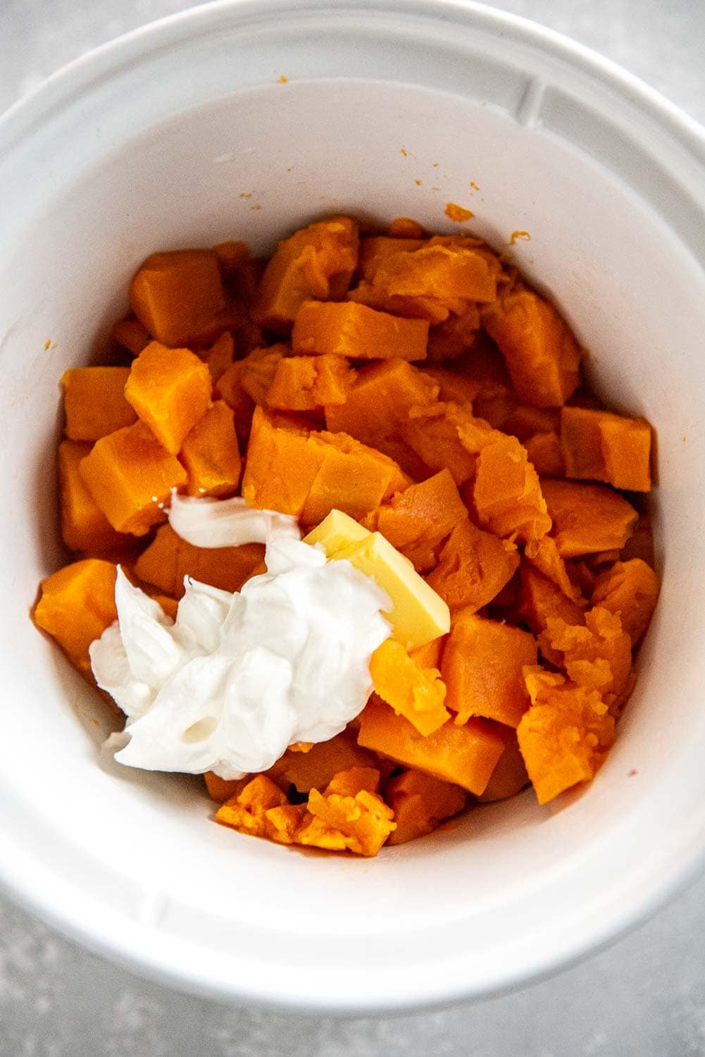 cubed sweet potatoes with butter and sour cream on top in slow cooker