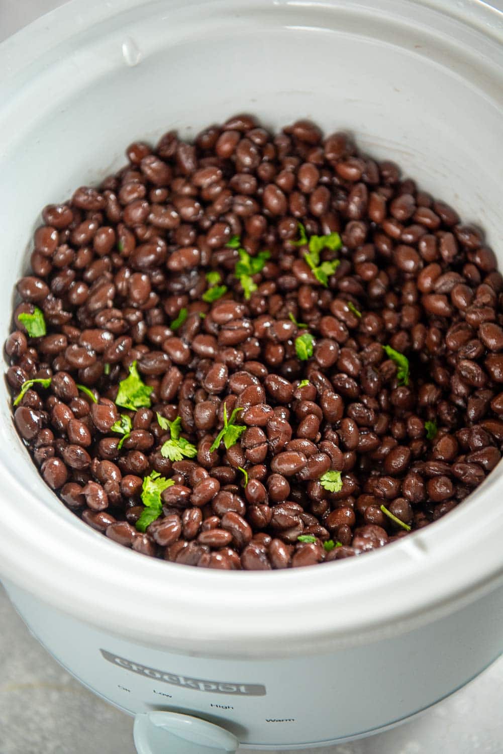 cooked black beans in white slow cooker with garnishings