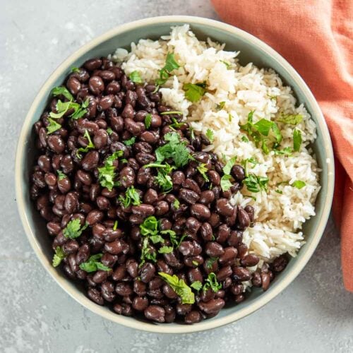 Bowl of white rice, cooked black beans, and garnished