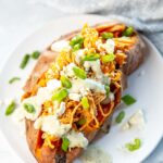 stuffed sweet potato with buffalo chicken, sauce, bacon, cheese, and green onions on top
