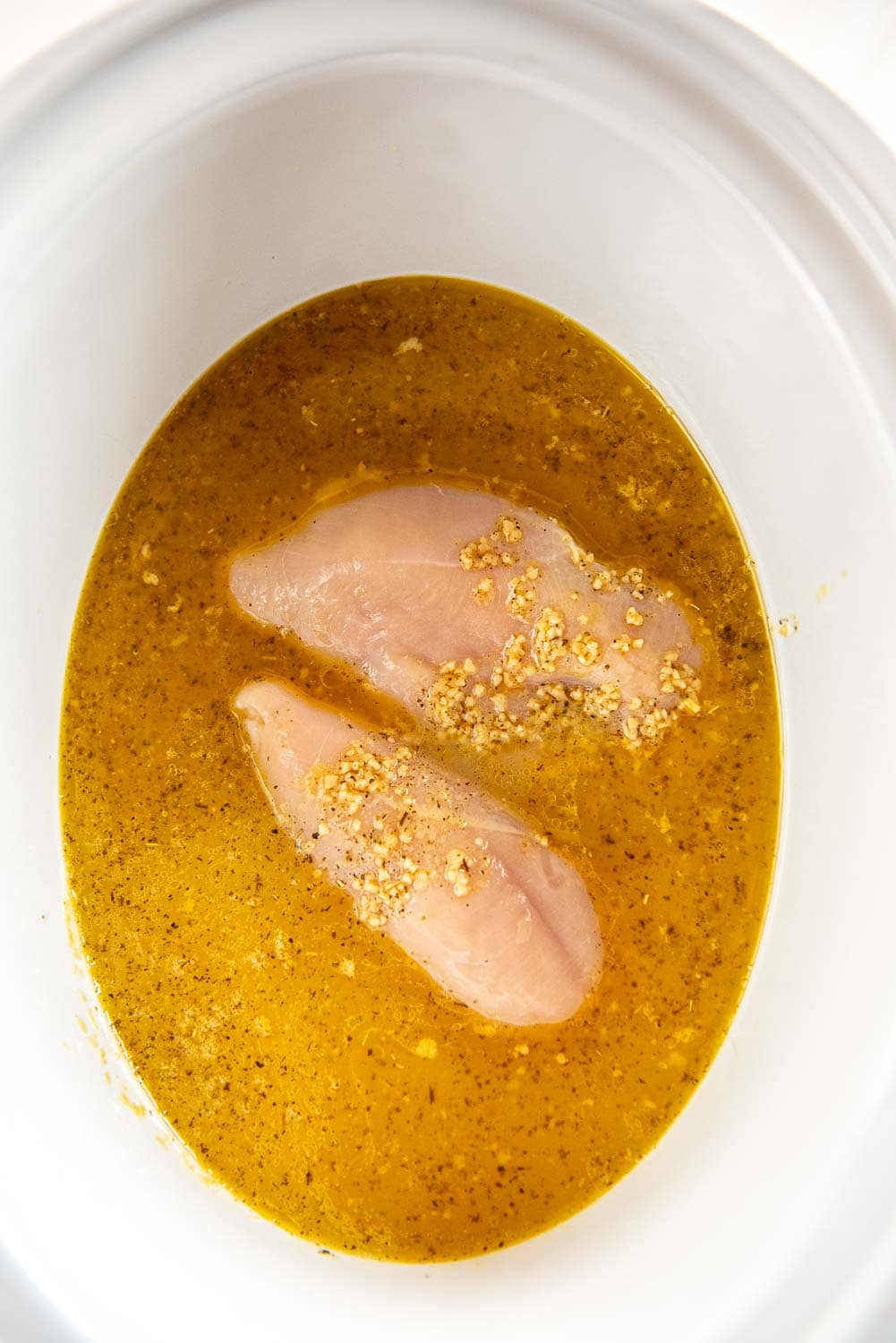Seasoned butter with garlic and seasonings in slow cooker with two chicken breasts inside