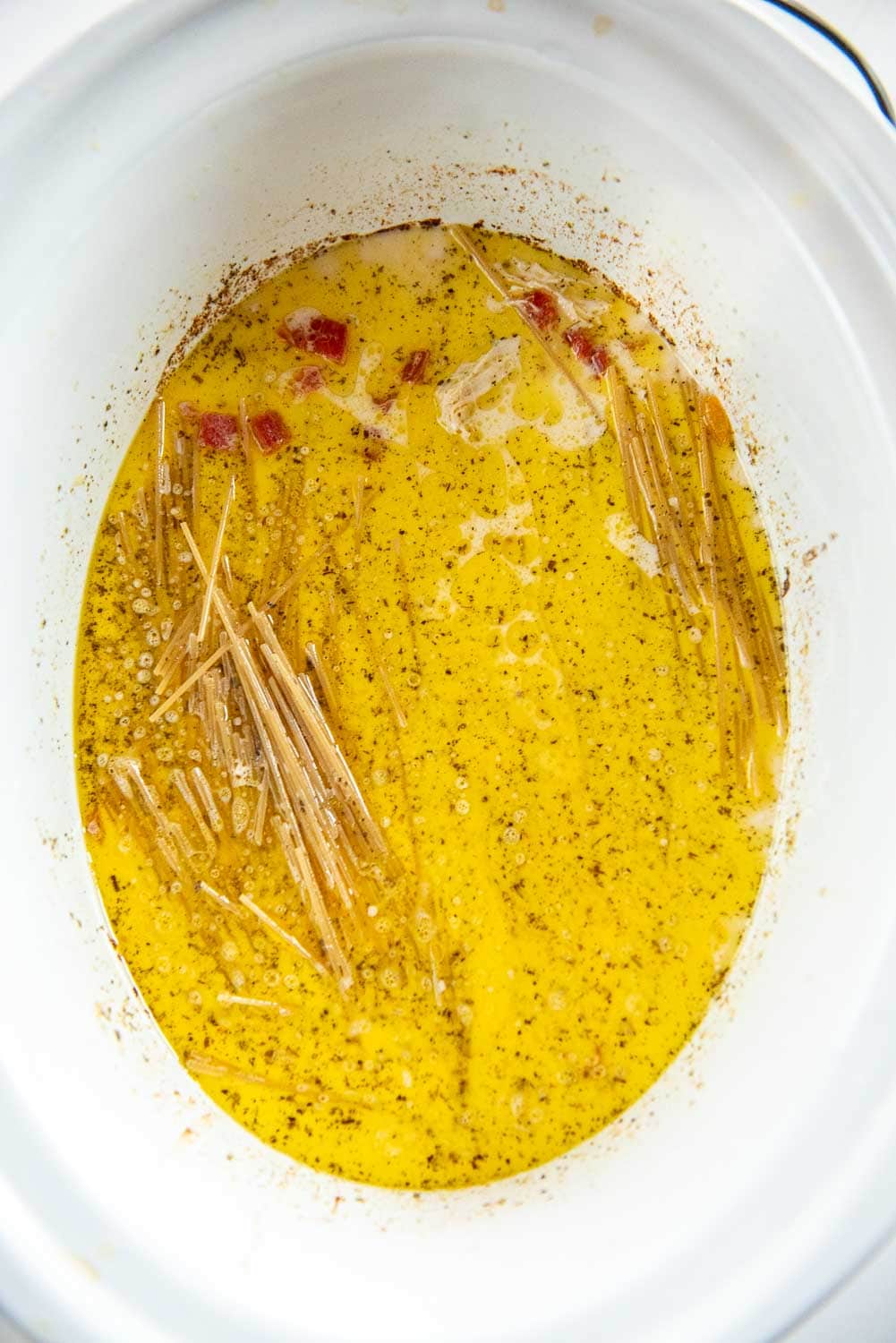 Seasoned butter mixture with uncooked spaghetti inside of slow cooker