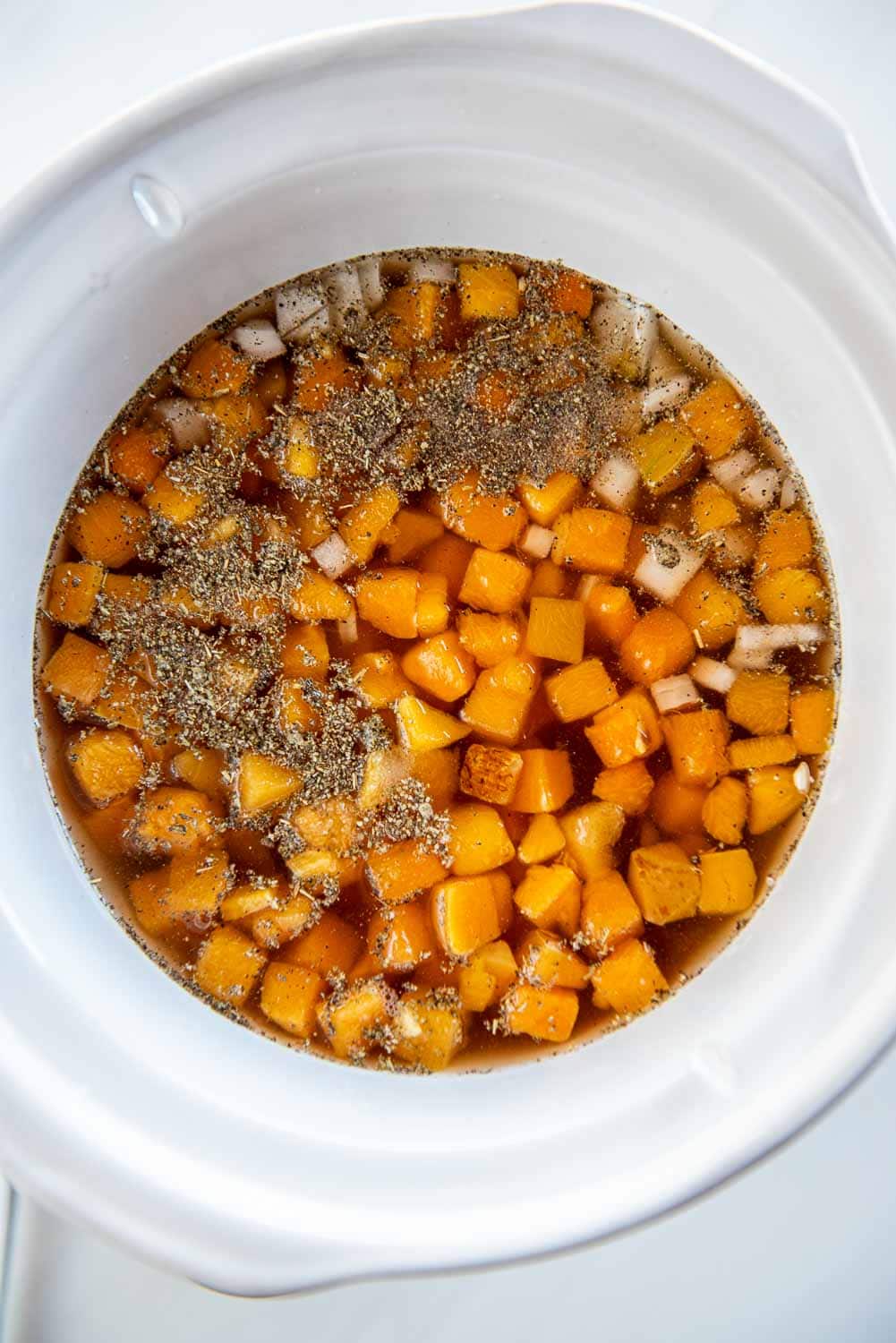 diced butternut squash in liquid with seasoning on top inside of slow cooker