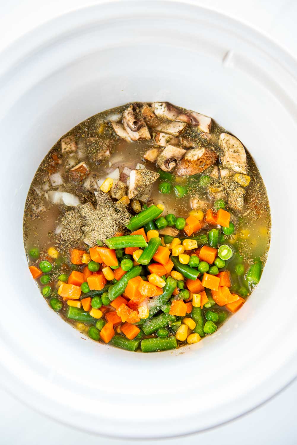 chicken breast with diced onions, mushrooms, mix of corn, green beans, carrots, seasonings inside of broth mix in slow cooker