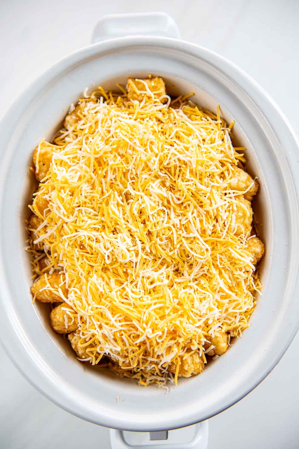 Extra crispy tater tots with shredded colby jack cheese on top inside of slow cooker