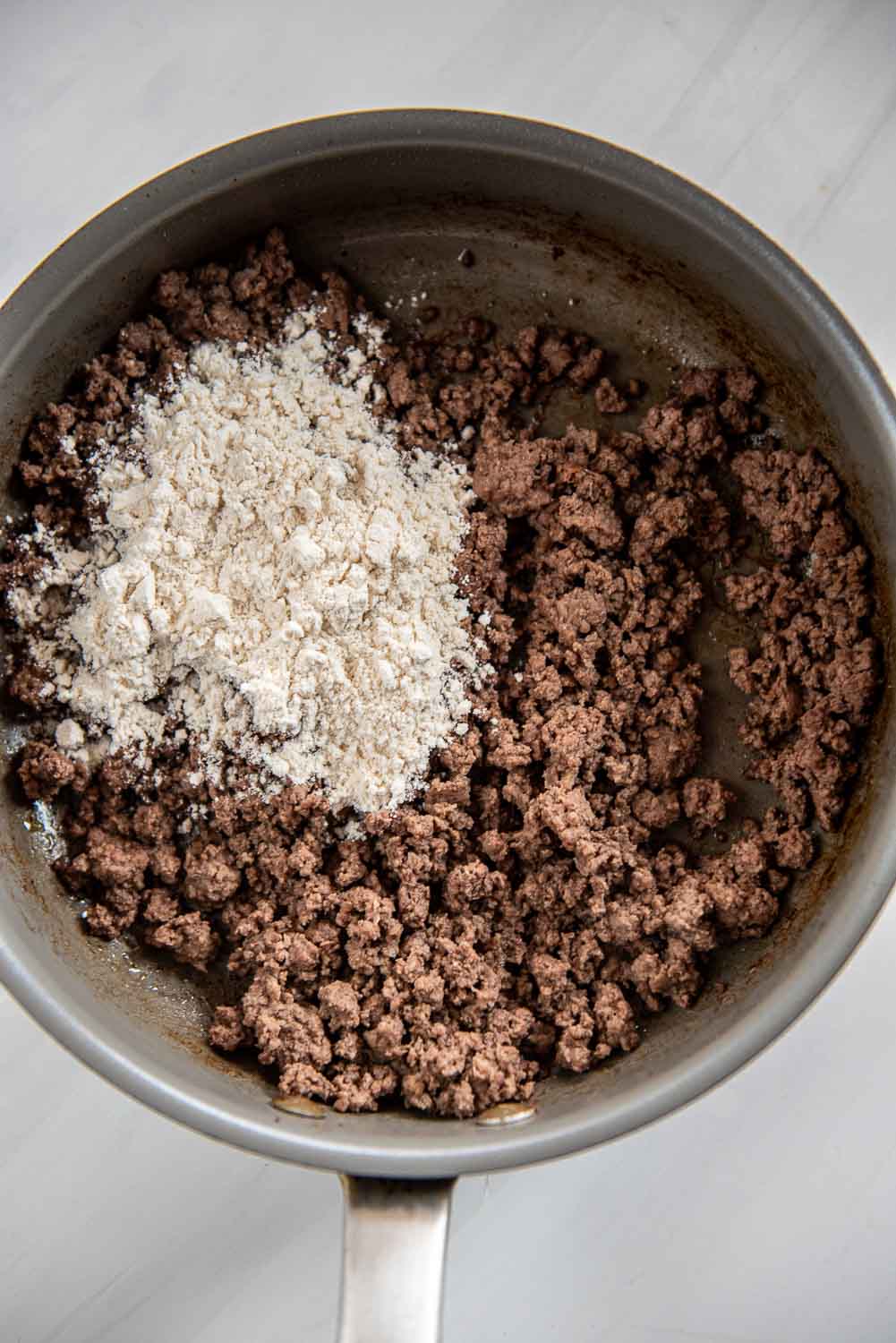 ground beef cooked in skillet with flour poured on top