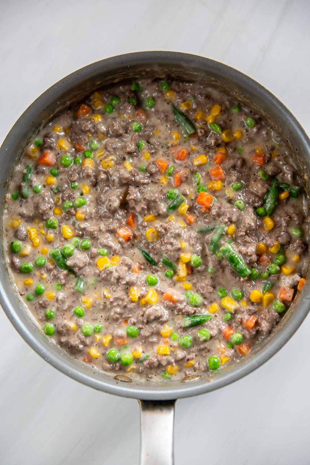 ground beef cooked and thickened with mixed vegetables like peas, green beans, and carrots in skillet