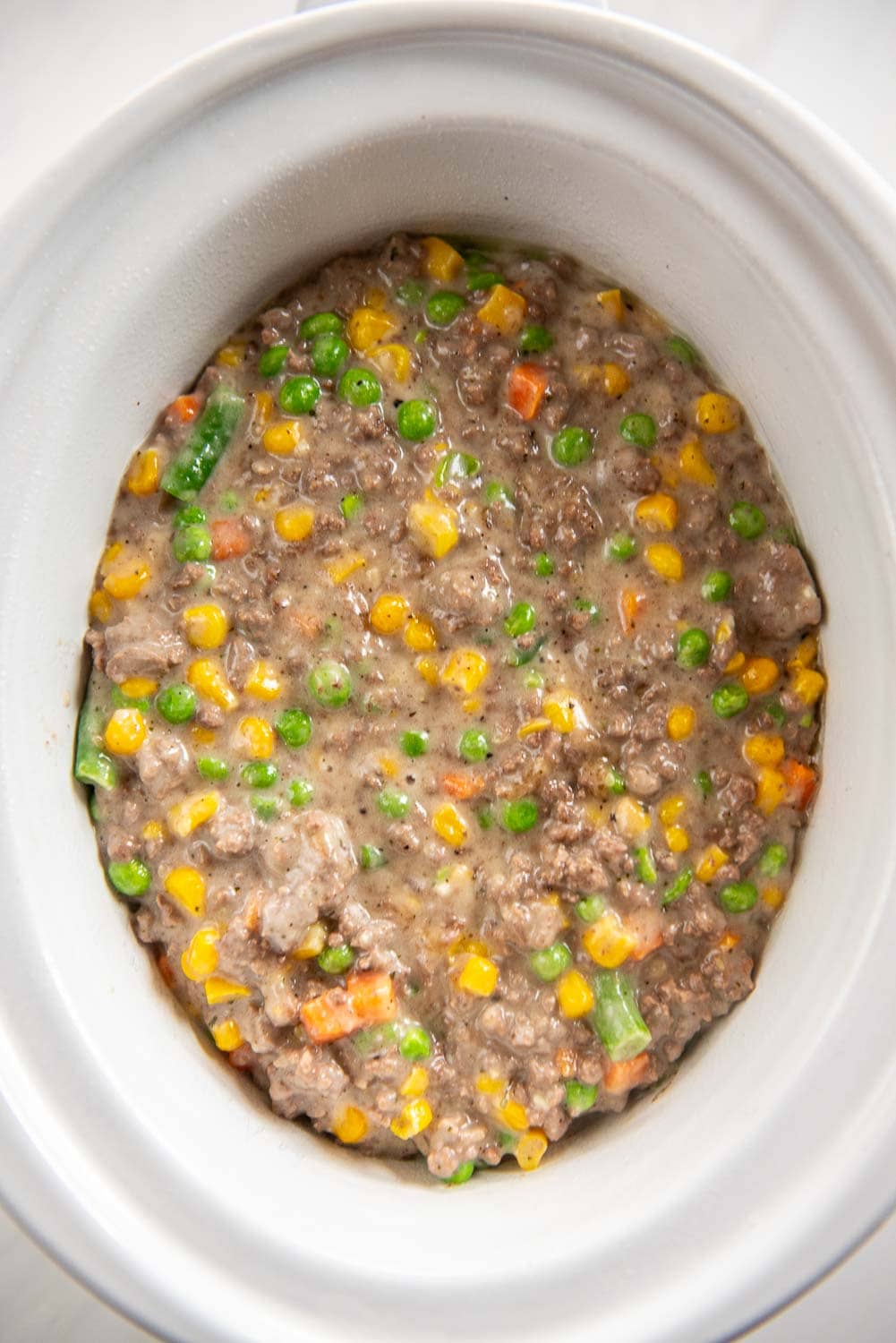 ground beef cooked and thickened with mixed vegetables like peas, green beans, and carrots in slow cooker