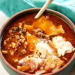Slow Cooker Lasagna Soup garnished with cheese and served in bowl with wooden spoon