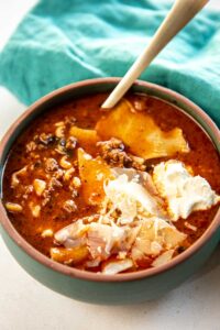 Slow Cooker Lasagna Soup garnished with cheese and served in bowl with wooden spoon