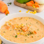 White shallow bowl of chowder with corn and sweet potatoes with green pepper, onion and sweet potato in background