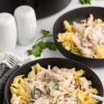 Slow Cooker Chicken Stroganoff served on black plate next to salt and pepper next to slow cooker