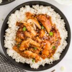 black bowl filled with rice topped with shredded teriyaki chicken topped with green onions and sesame seeds
