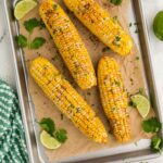 Slow Cooker Corn on the Cob on baking dish with parchment paper next to slices of lime