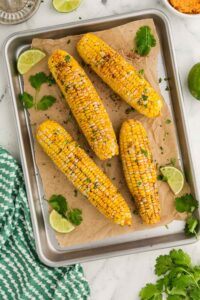 Slow Cooker Corn on the Cob on baking dish with parchment paper next to slices of lime