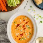 Cheesy Slow Cooker Buffalo Chicken Dip garnished and in bowl next to dish of celery, carrots, and tortilla chops