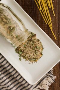Seasoning shaker with Homemade Spaghetti Seasoning Recipe with some of the mixture being pouted onto the plate