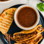 2 birria tacos plates with sauce and served