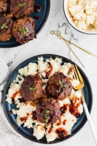 blue plate of mashed potatoes topped with three meatballs drizzled with bbq sauce