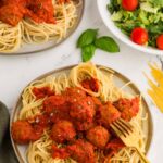 two plates filled with spaghetti topped with meatballs and red sauce next to a tossed salad in a white bowl