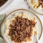 two white plates with mashed potatoes an shredded beef