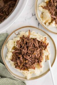 two white plates with mashed potatoes an shredded beef