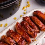bbq country ribs on white platter next to bowl of corn and black slow cooker