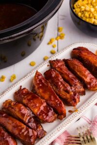 bbq country ribs on white platter next to bowl of corn and black slow cooker