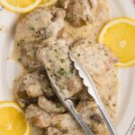 Slow Cooker Chicken Thighs With A Creamy Lemon Sauce cooked and served on dish with lemon for garnish tongs picking up recipe