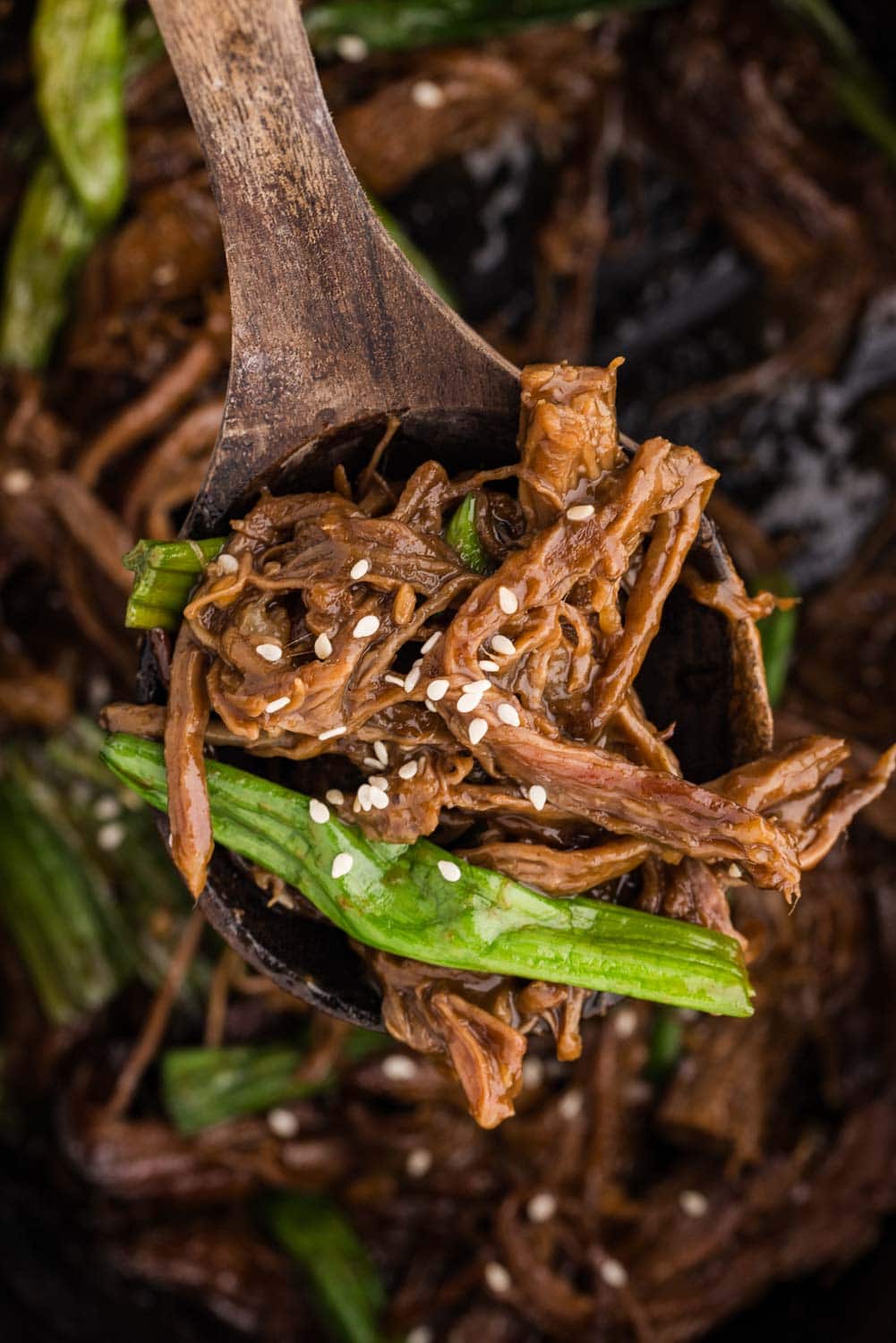 Close-up of a fork lifting tender shredded Mongolian beef, garnished with freshly sliced green onions