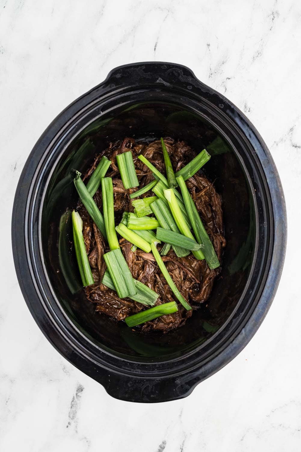 Shredded mongolian beef with green onions laid on top in slow cooker