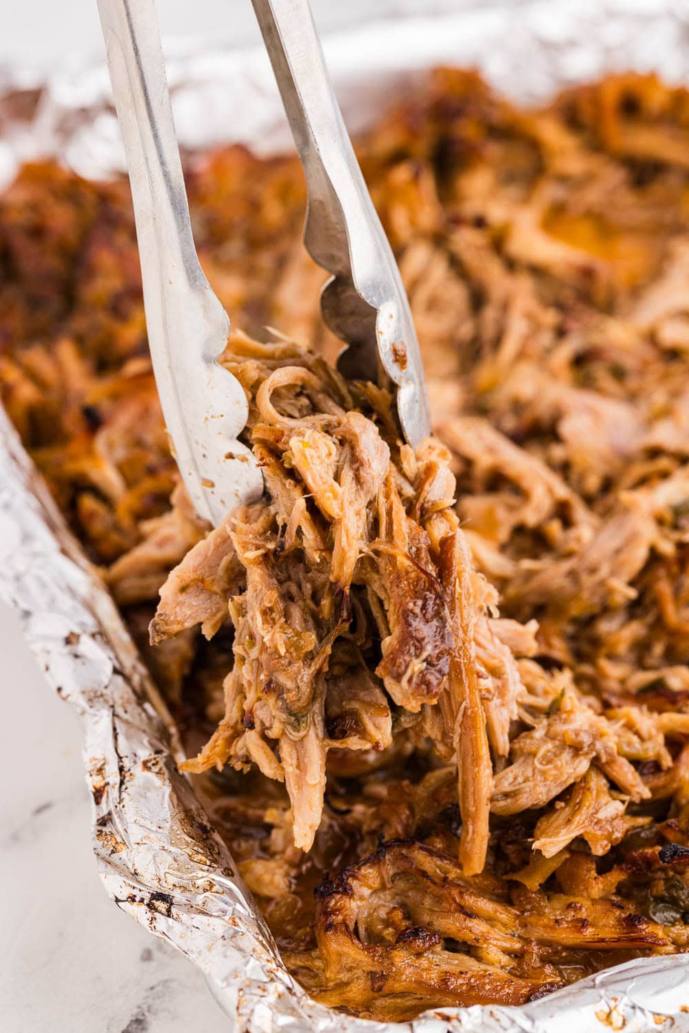 Slow Cooker Carnitas being picked up by tongs