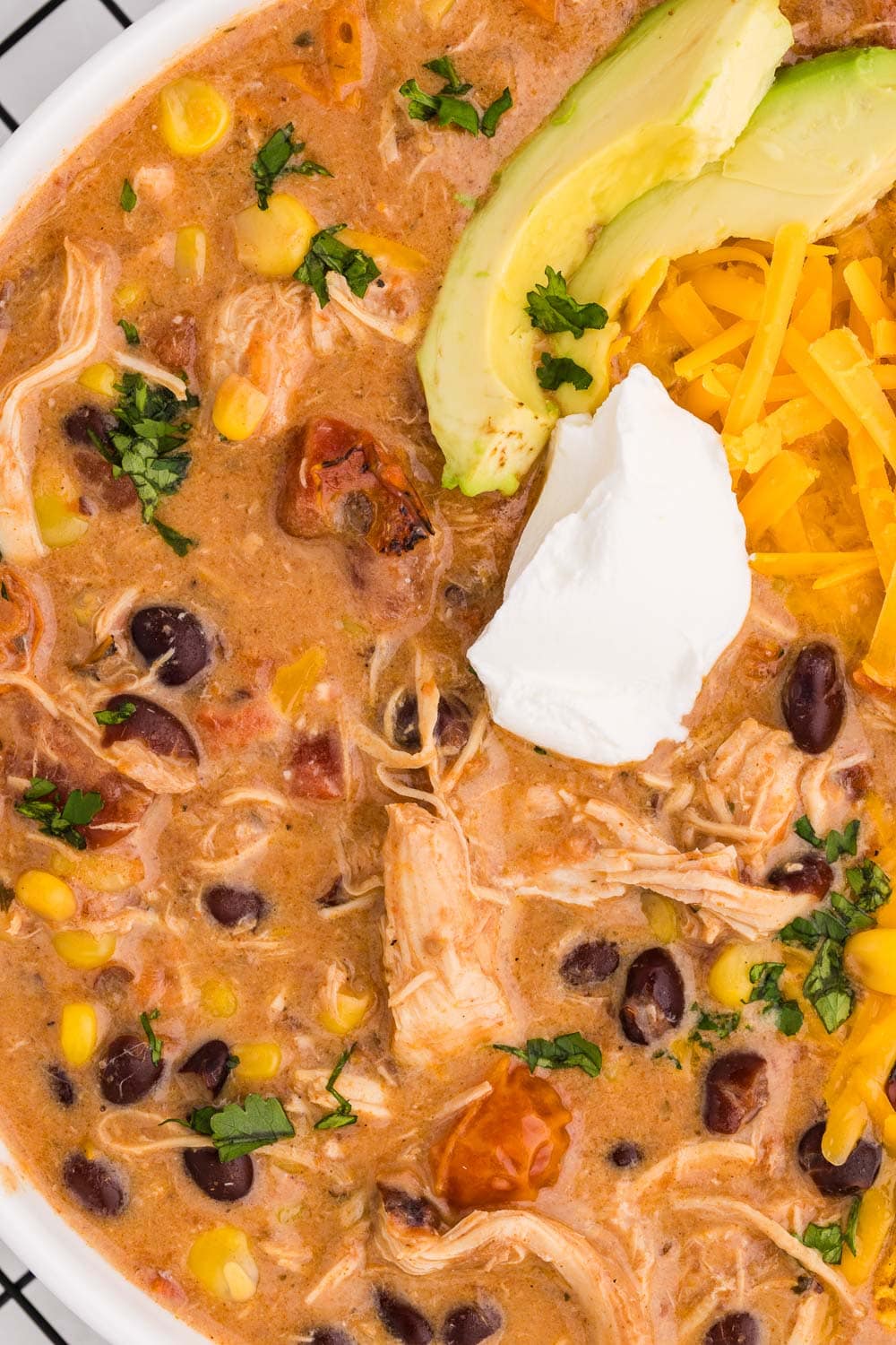 Close up of Slow Cooker Creamy Chicken Enchilada Soup served and garnished with sour cream and avocado