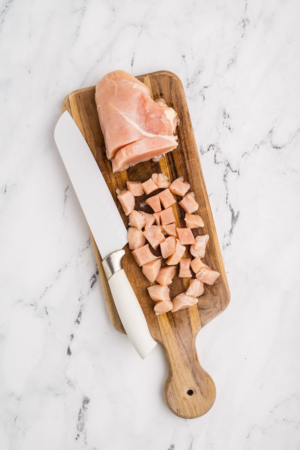 Chicken breast being diced on cutting board