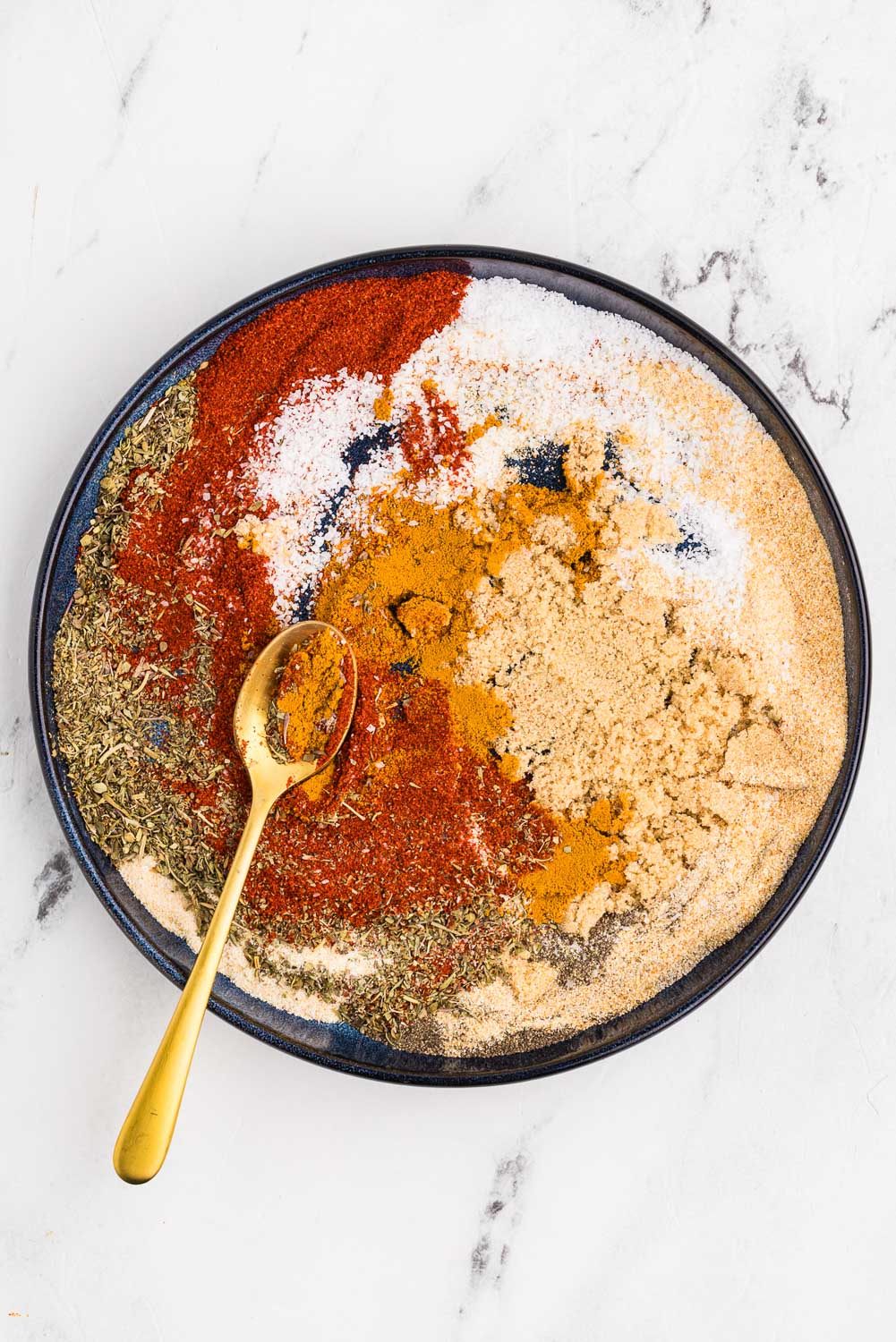 Ingredients like 2 tablespoons sweet paprika 1 tablespoon Italian seasoning 1 tablespoon kosher salt 1 tablespoon onion powder 1 tablespoon garlic powder 1 tablespoon brown sugar 2 teaspoons turmeric 2 teaspoons black pepper 1 teaspoon celery salt ready to be mixed together in bowl with spoon