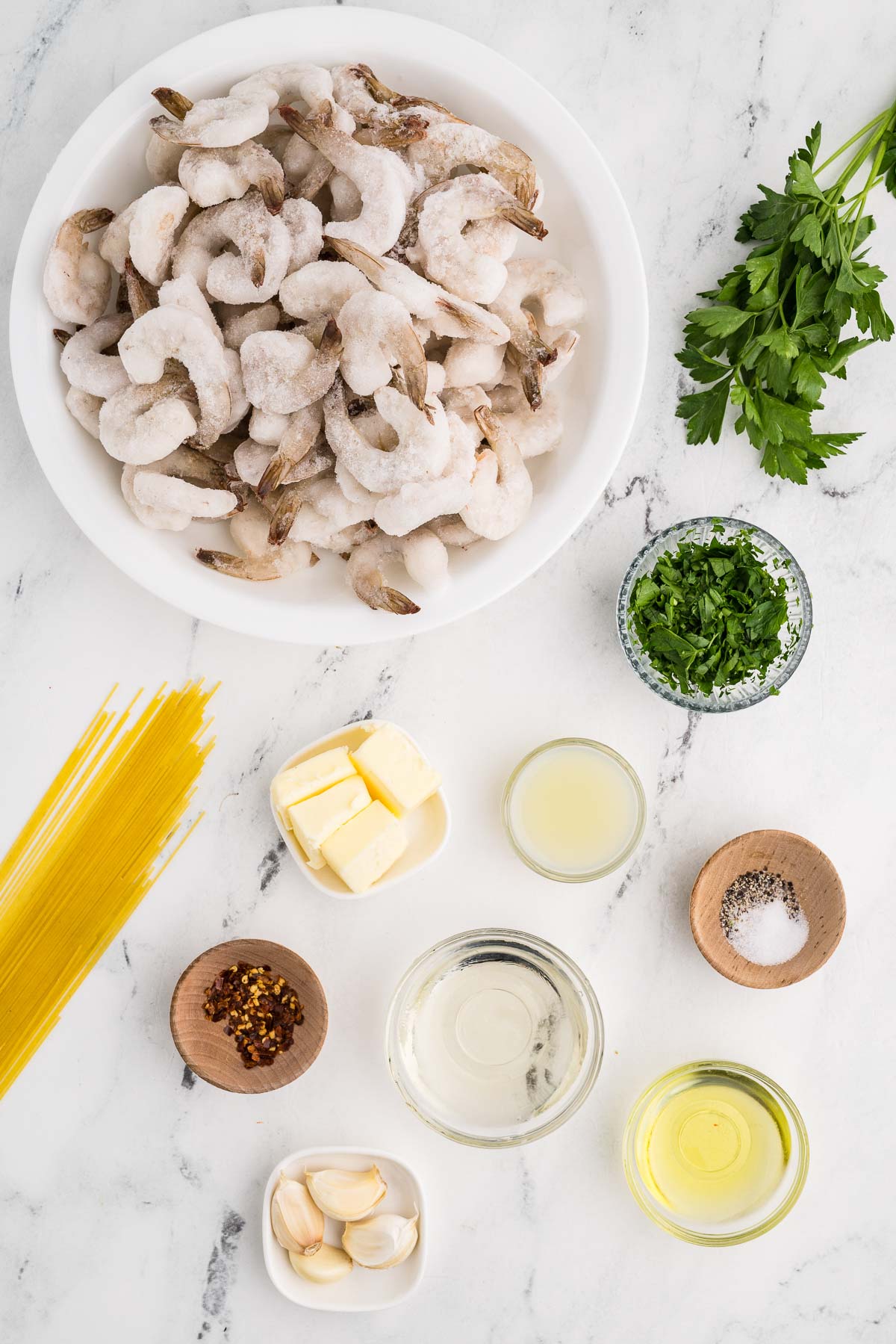 24 oz frozen shrimp, peeled, deveined (tail-off optional) 2 tablespoons olive oil 4 tablespoons butter, sliced into 4 pieces ¼ cup white wine 4 cloves garlic, finely minced ¼ teaspoon salt ⅛ teaspoon pepper Pinch of red pepper flakes 2 tablespoons lemon juice Fresh chopped parsley Cooked angel hair pasta or bread on counter