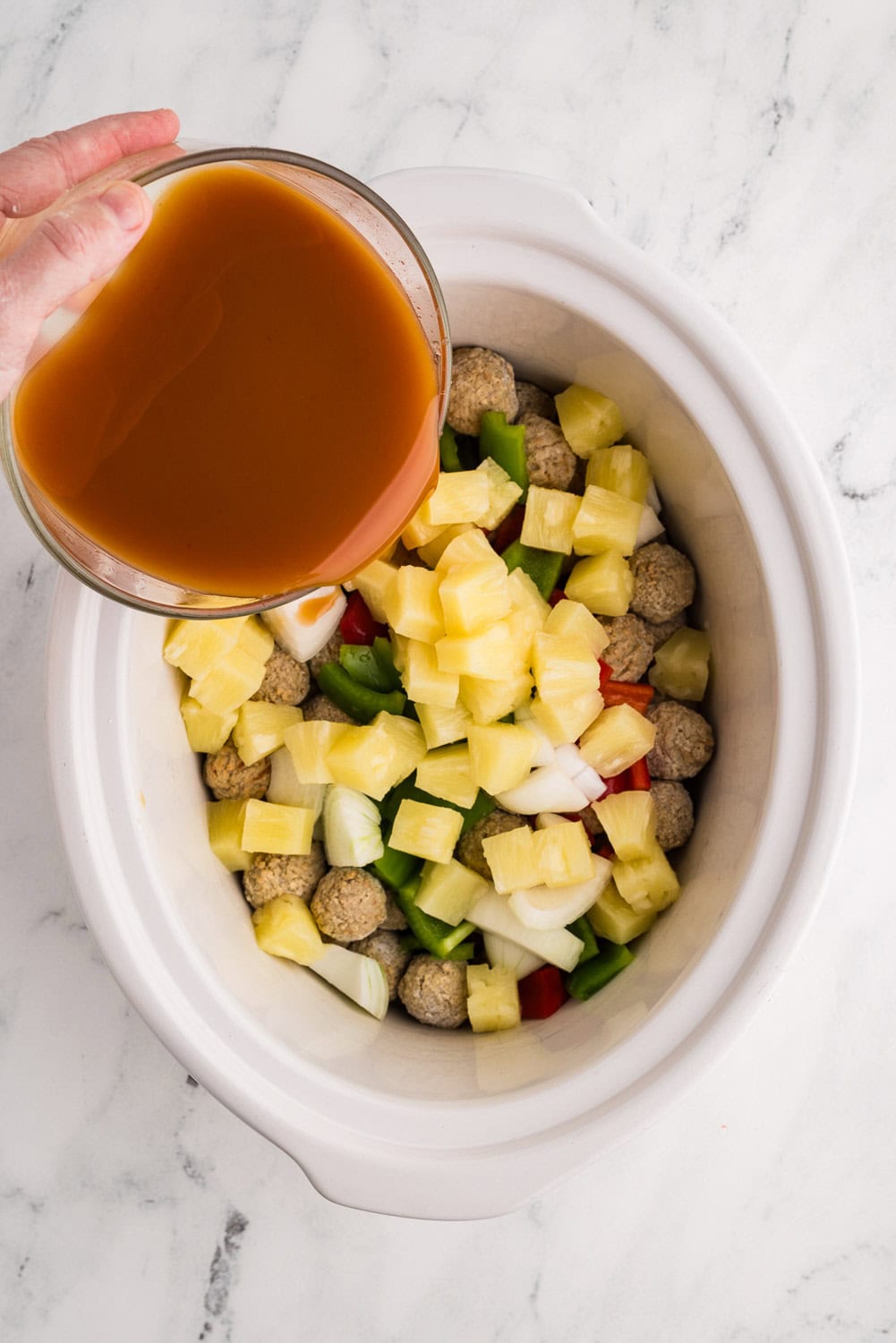 Pouring mixture of sweet and sour sauce over the meatballs in slow cooker