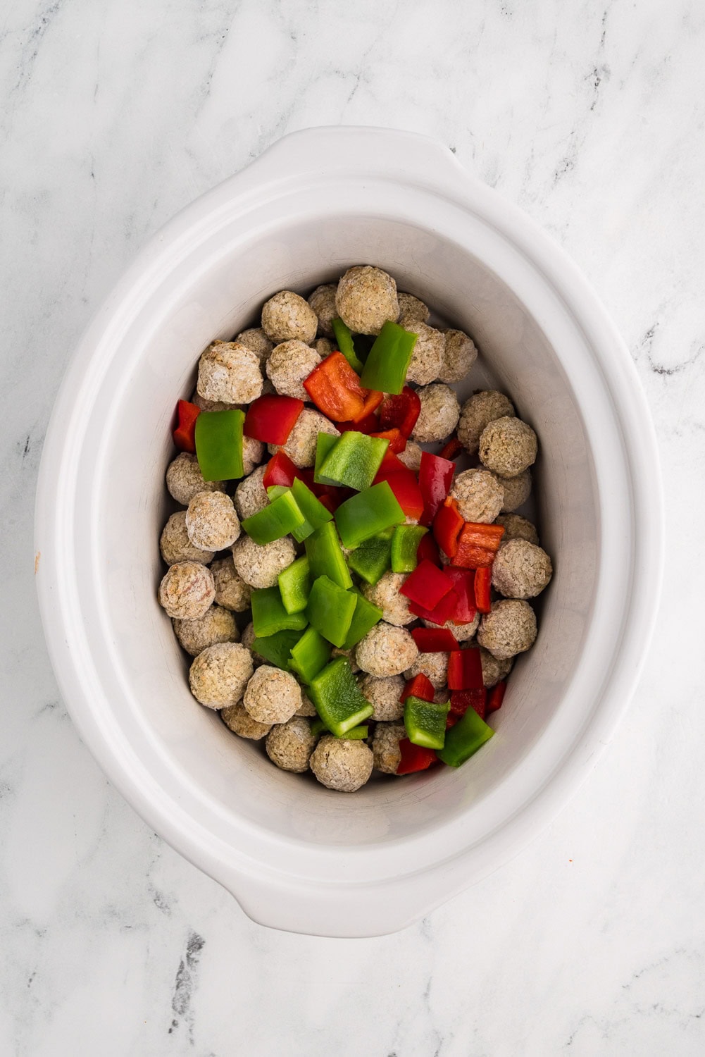 Frozen Meatballs and chopped red and green peppers laid on top inside of slow cooker