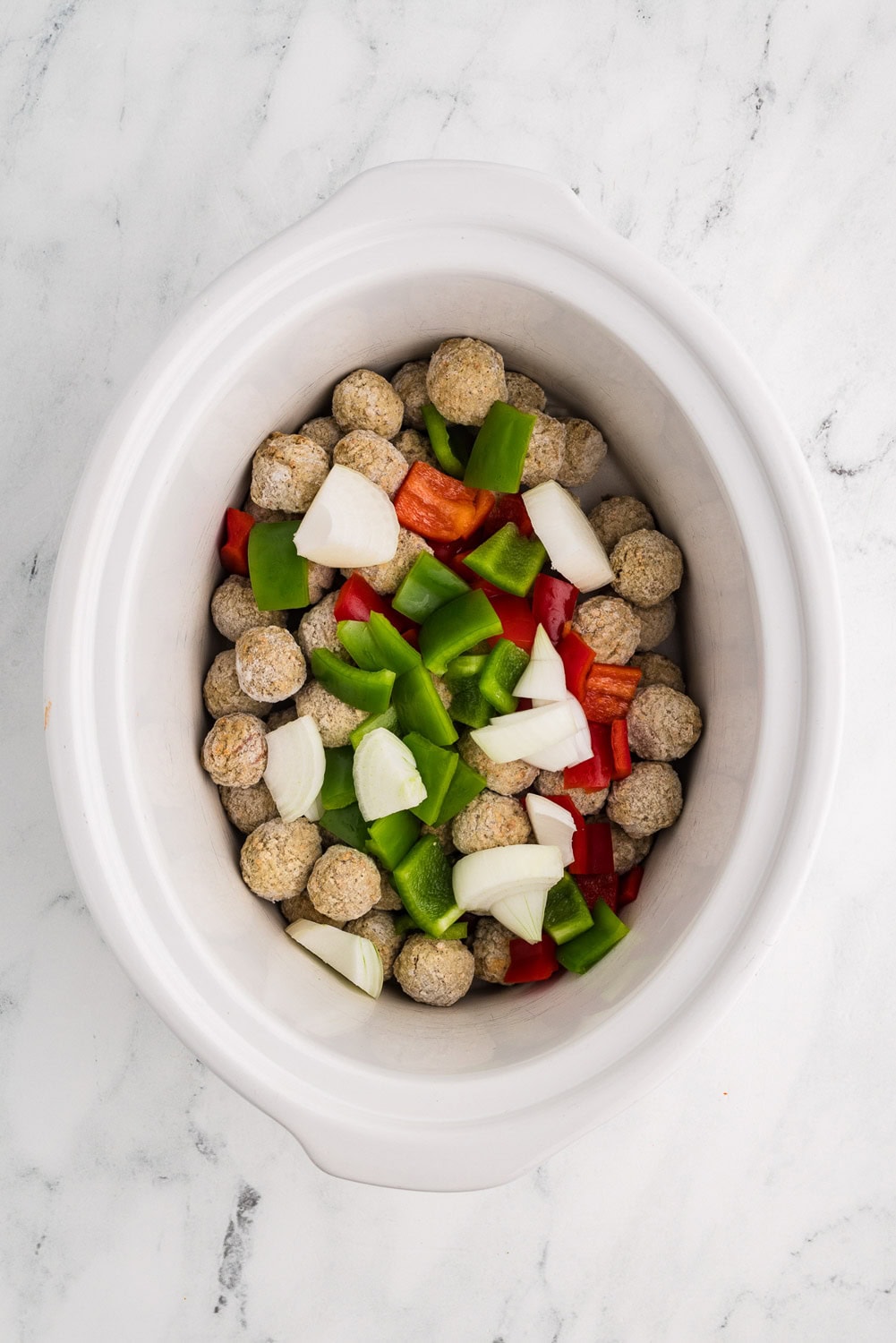 Frozen Meatballs and chopped red, green peppers, and chopped onions laid on top inside of slow cooker