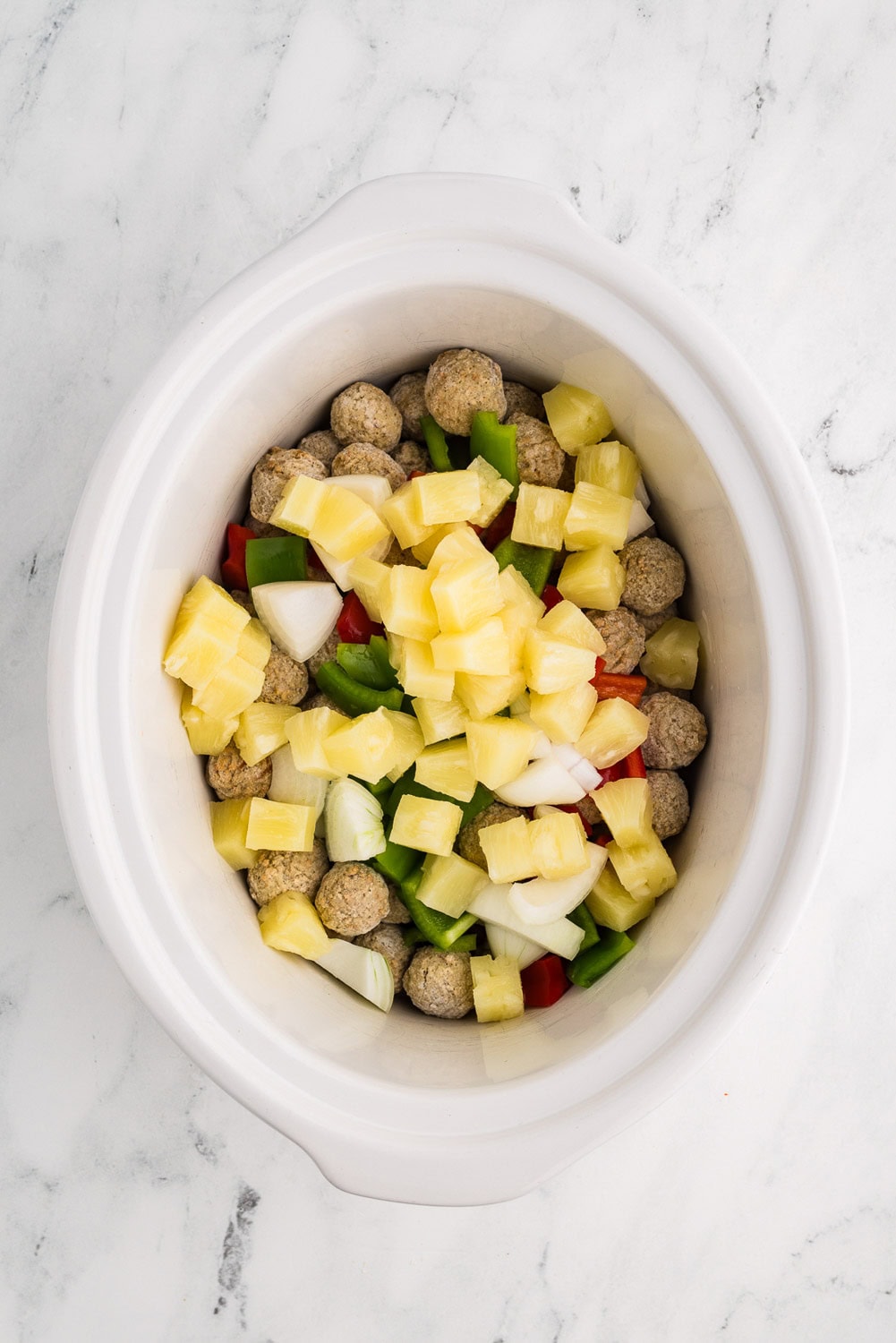 Frozen Meatballs and chopped red, green peppers, onions, and diced pineapples inside of slow cooker