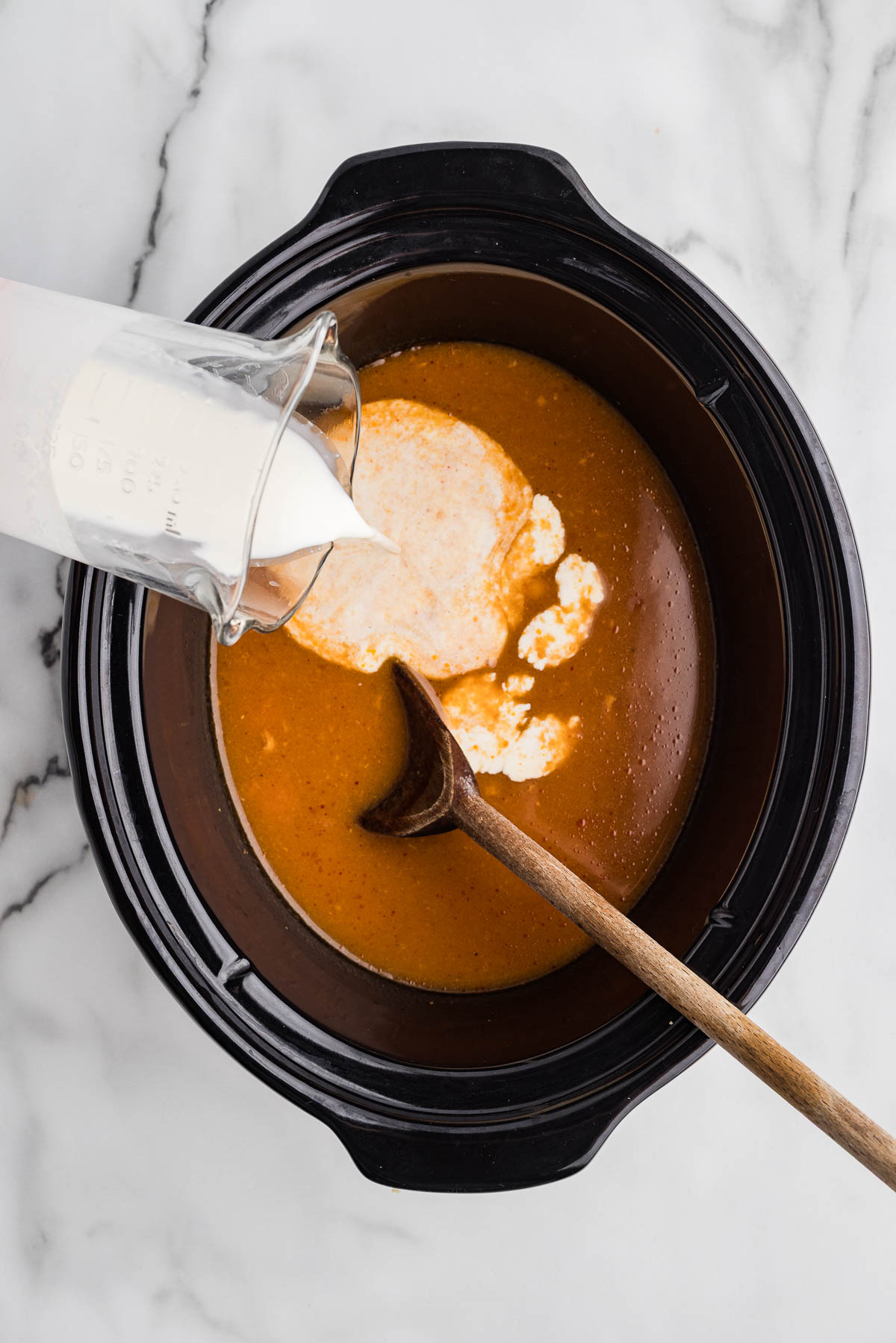 Mixed firecracker chicken mixture and heavy cream being mixed into slow cooker