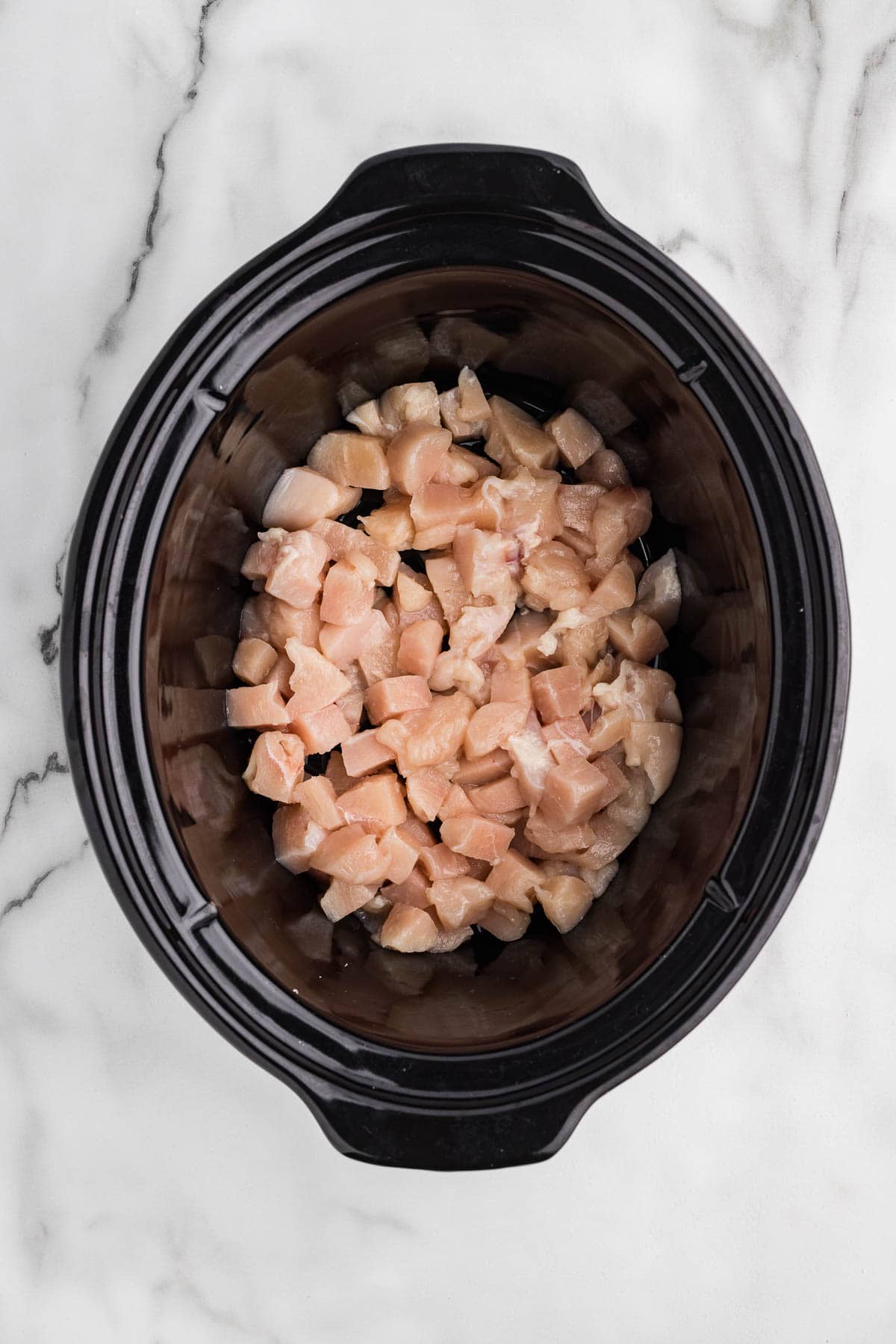 Raw diced chicken in slow cooker ready to cook