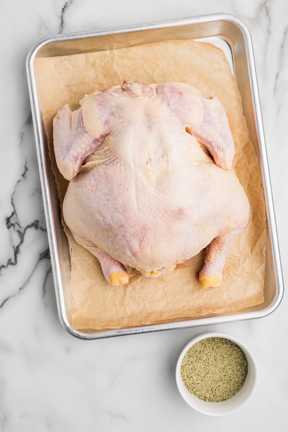 Whole chicken on parchment paper on pan
