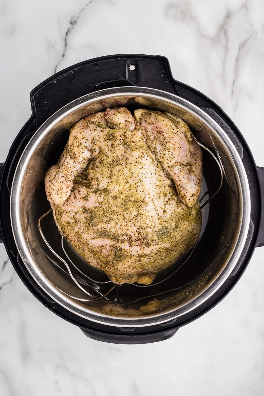Whole chicken seasoned sitting on trivet in instant pot