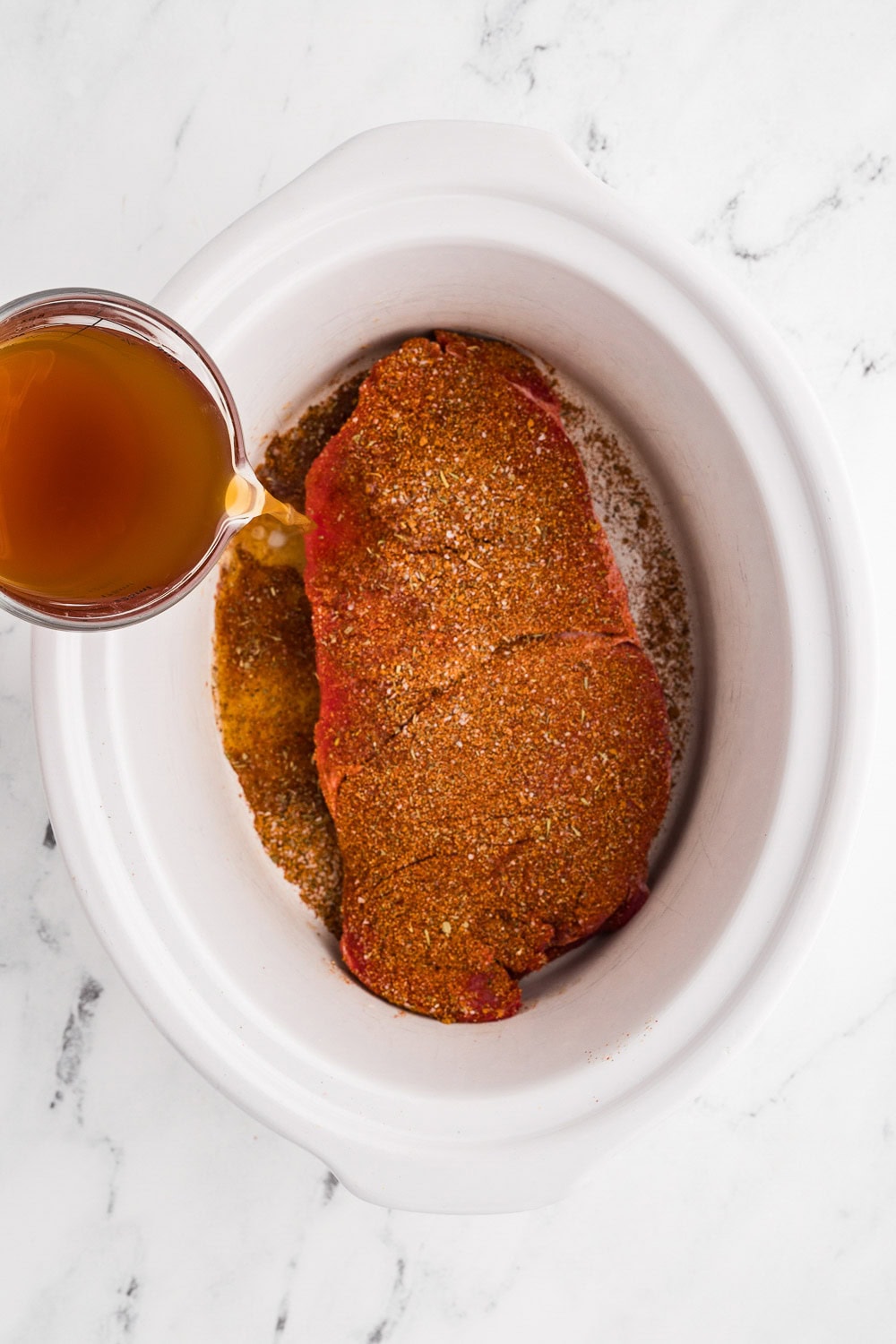 2 pound top round roast (london broil) with chicken broth being poured on top