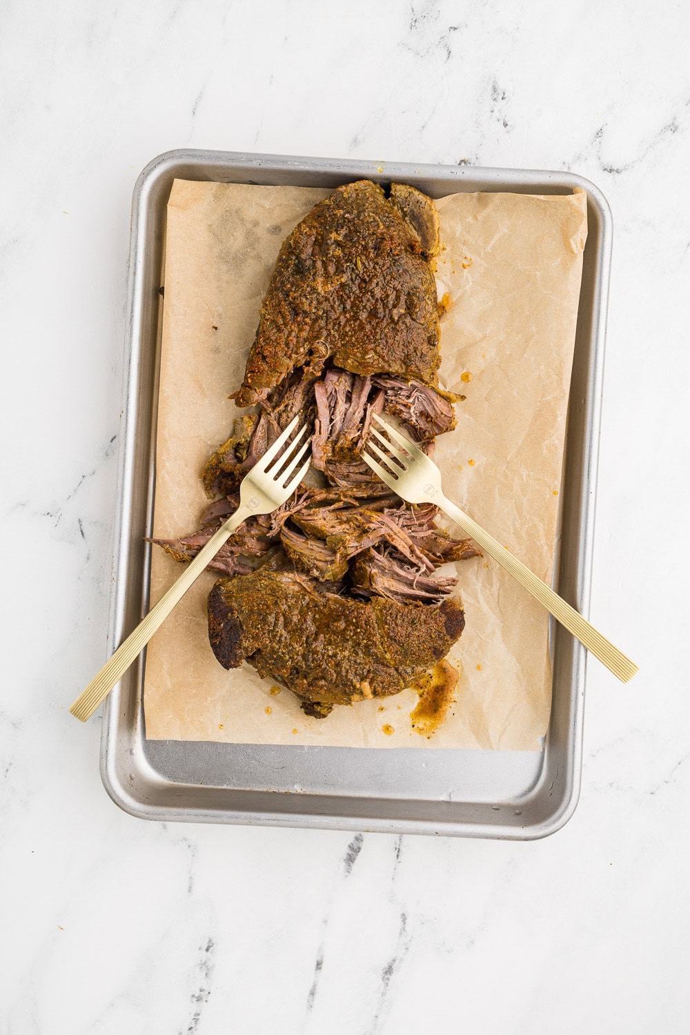 Slow Cooker London Broil being shred on baking dish on parchment paper with 2 forms