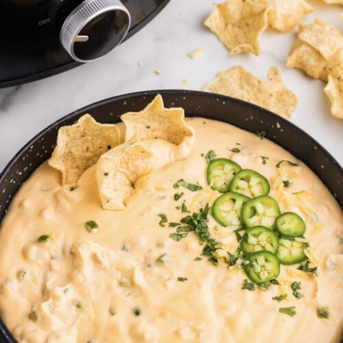 Slow cooker queso in a black bowl with chips