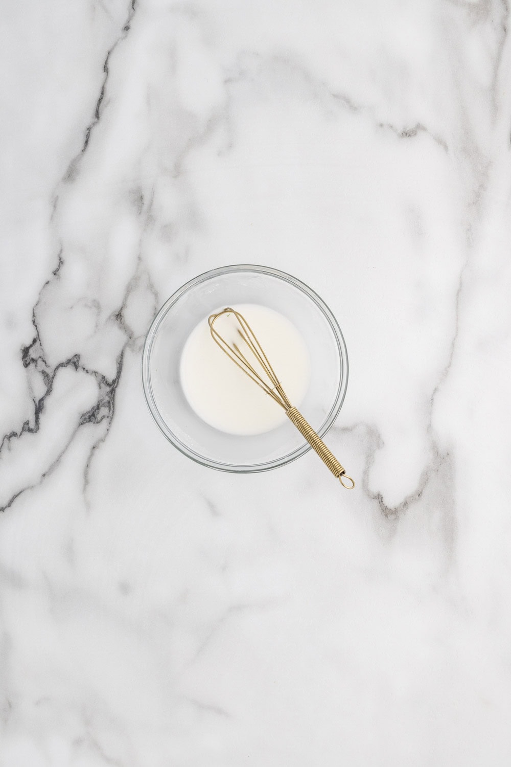 A whisk and a bowl of cream on a marble counter